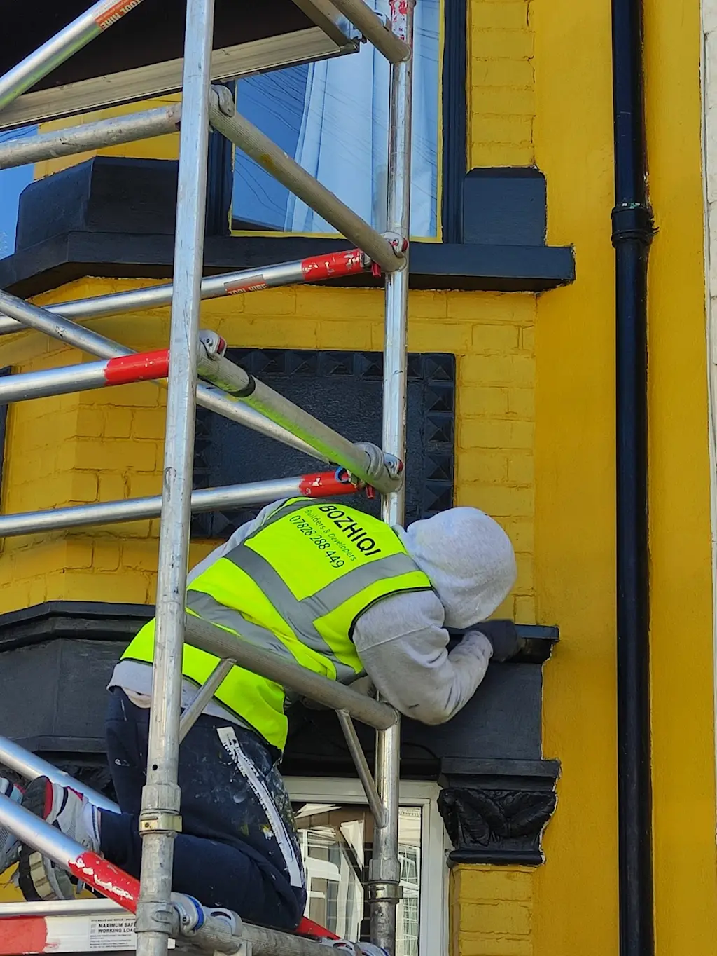 Bozhiqi decorator on scaffolding painting Victorian terraced house exterior