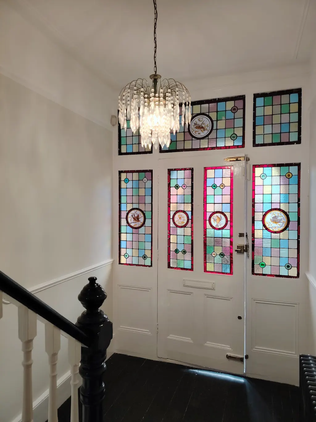 Period hallway with freshly painted white walls and black woodwork, stained glass door
